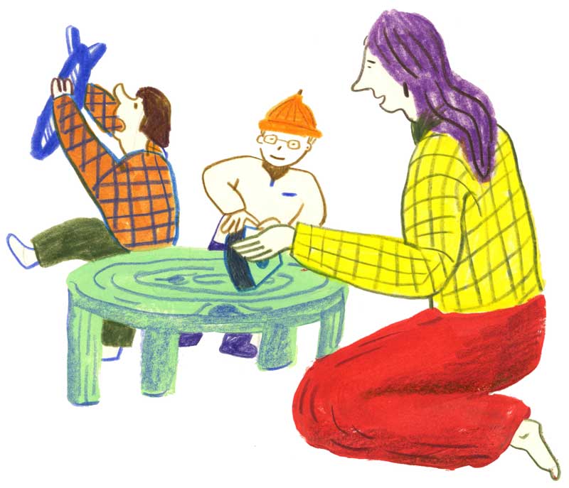 Bild: Eine junge Frau spielt mit zwei Kindern an einem niedrigen Tisch.